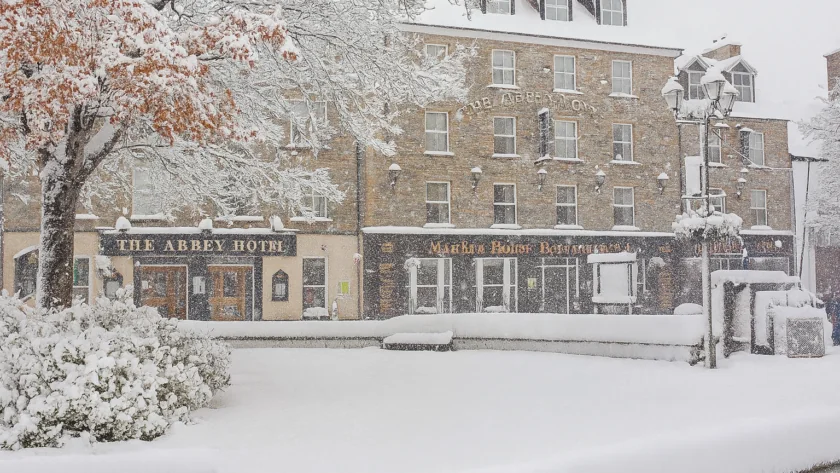 A hotel and restaurant building on a street covered in heavy snow, with snow-laden trees and bushes in the foreground.