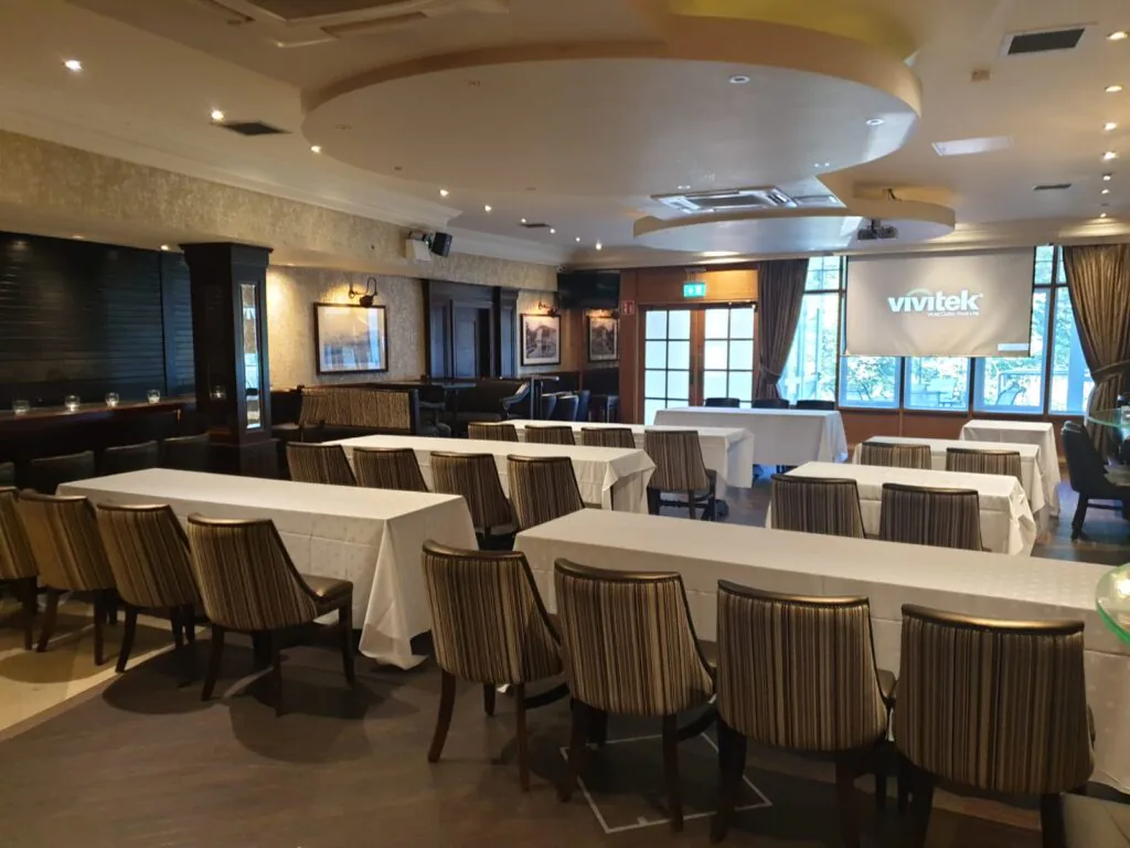 Stylish Hotel Conference Room Elegant conference room with long tables, striped chairs, projector screen, and warm lighting at a luxurious hotel.